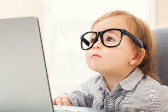 Smart toddler girl wearing big glasses while using her laptop