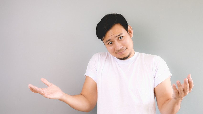 Rasing his shoulder and arms as he does not care. An asian man with white t-shirt and grey background.