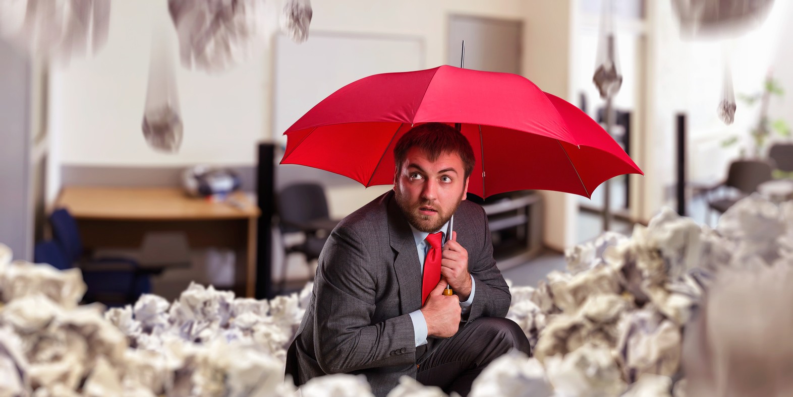 Scared businessman with umbrella protecting from papers in the office