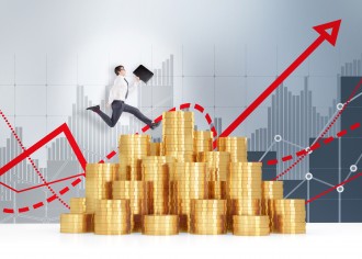 Young businessman with a black folder in hand running over a heap of golden coins, red graphs and grey bar charts behind. Grey background. Concept of making money.